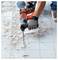 'A person uses a power tool to remove tiles from a floor, resulting in broken pieces scattered around. The tool is held with gloves.'