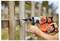 Person using an orange and grey Black+Decker drill to make a hole in a wooden fence. Background shows more wooden fences.