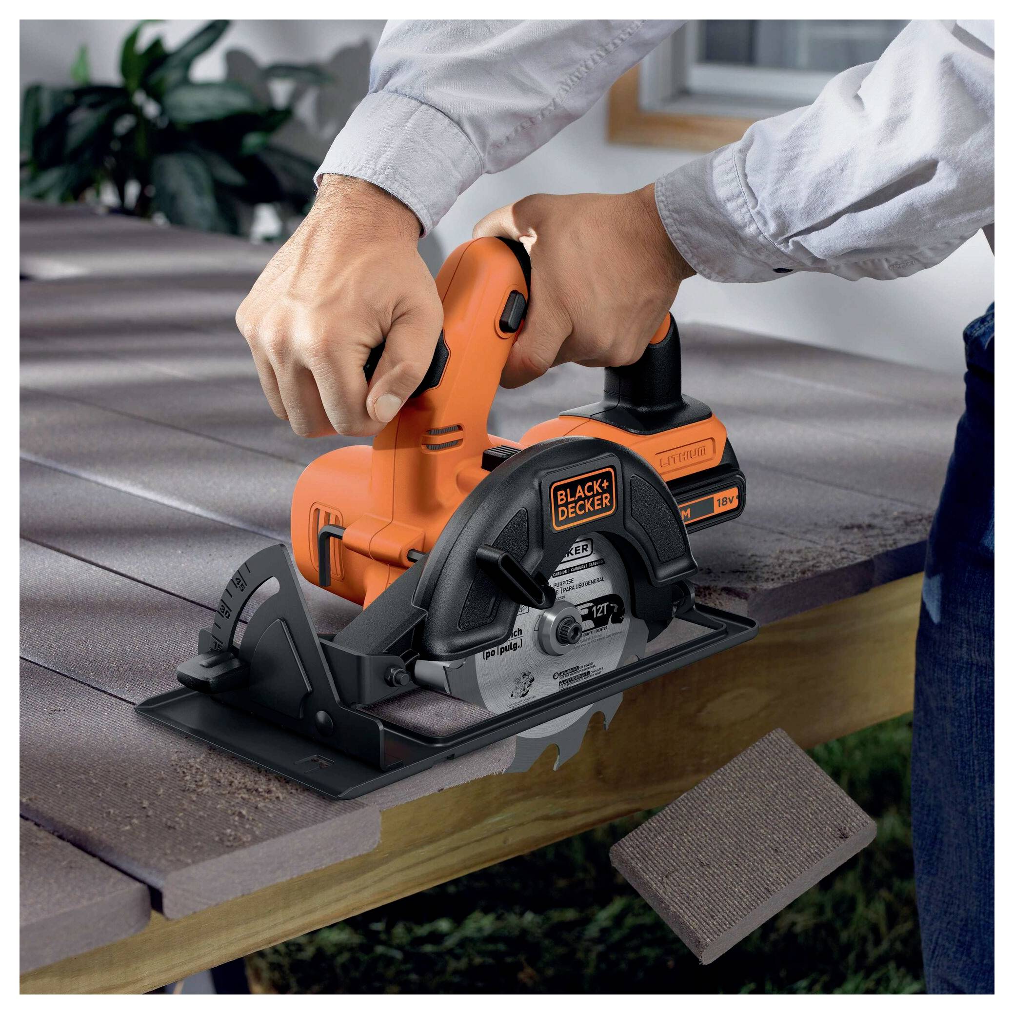 A person is using an orange and black electric saw to cut brown composite decking. A sanding sheet is shown in the corner.
