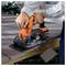A person is using an orange and black electric saw to cut brown composite decking. A sanding sheet is shown in the corner.