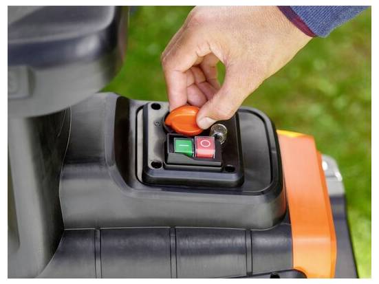 A hand is turning an orange key in an ignition switch with green 'on' and red 'off' buttons, likely on a piece of machinery.