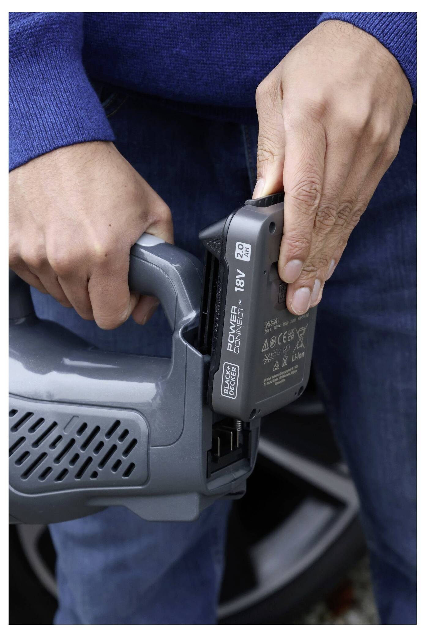 A person is inserting an 18V battery into a handheld power tool, demonstrating the process of equipping the tool for use.