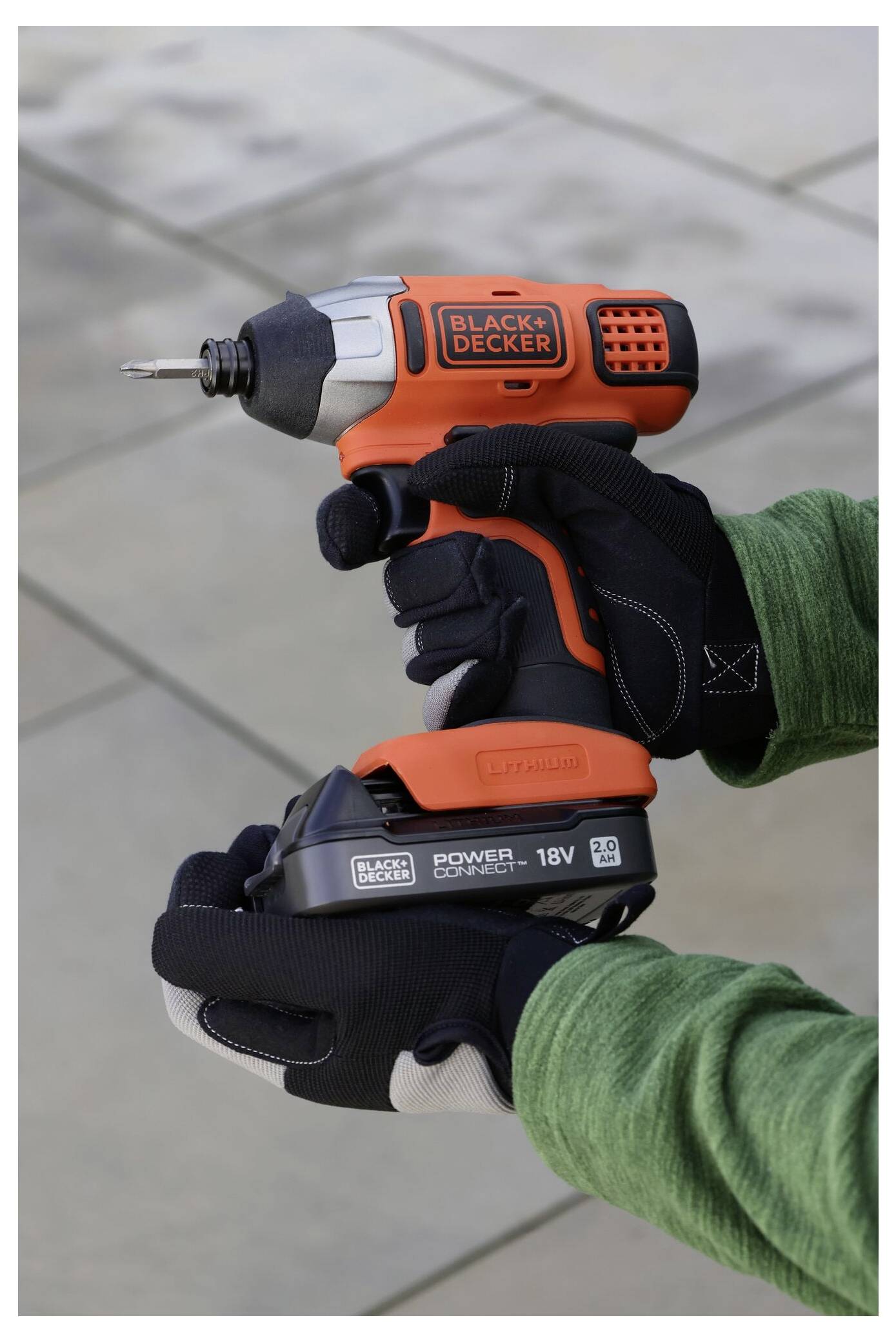 A person holding an orange and black electric drill with gloved hands, labeled 'Black & Decker', on a tiled background.
