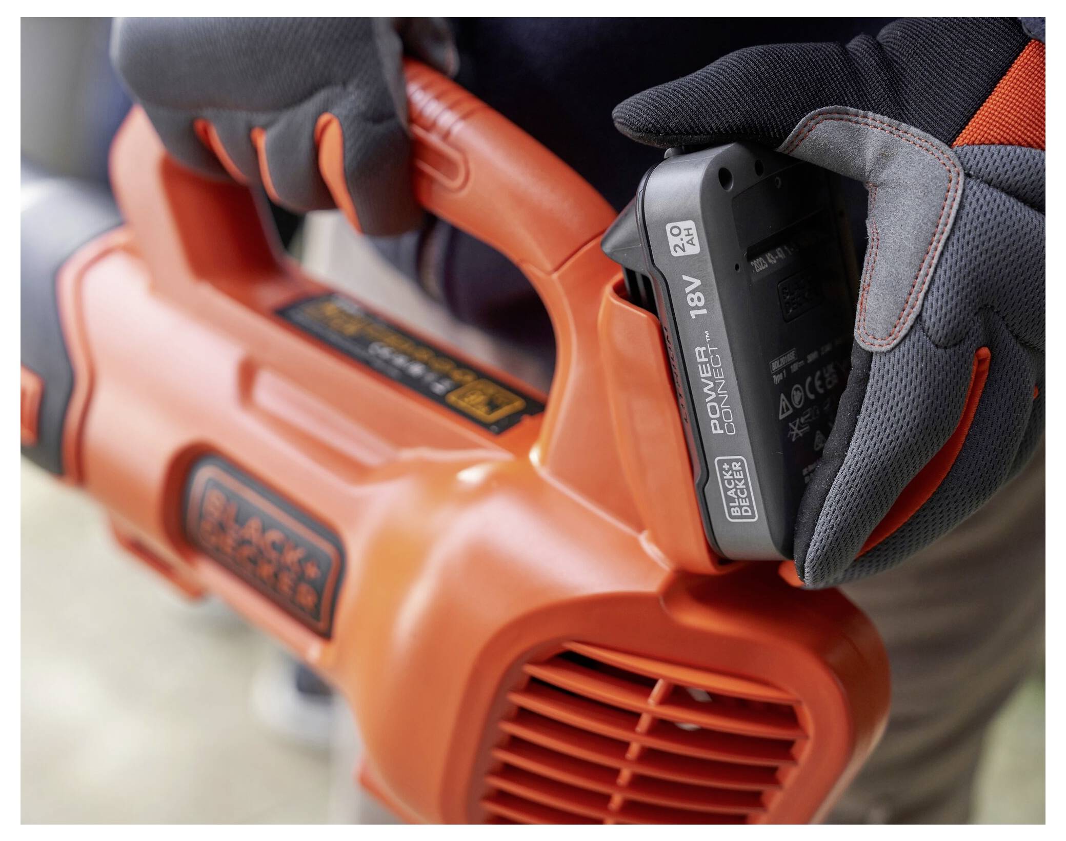 'A person wearing gloves inserts an 18V battery into an orange power tool, emphasizing safe handling and preparation before use.'