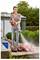 A person uses a power washer to clean red soccer cleats on a stone ledge outside a house with greenery in the background.