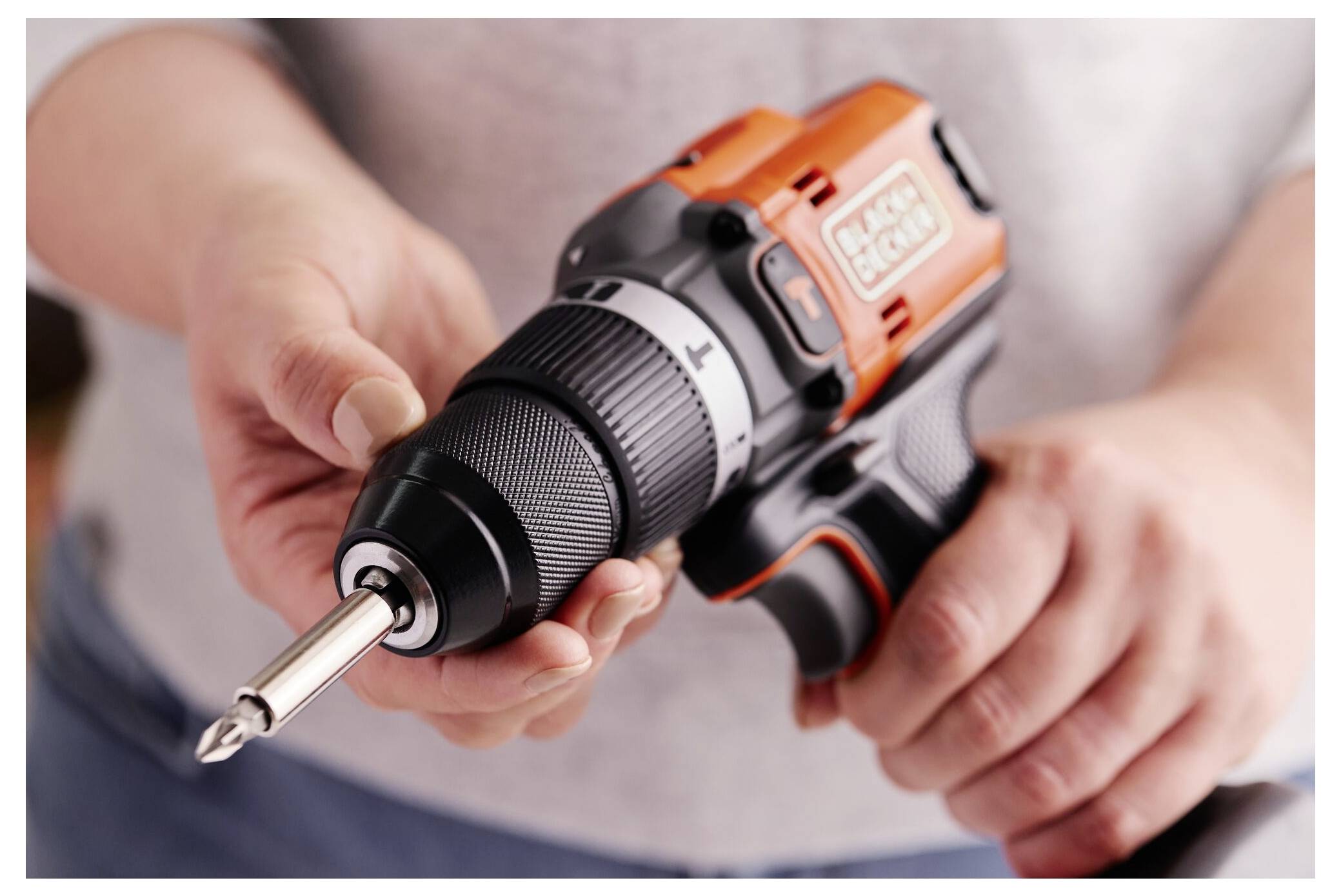 A person holds an orange and black cordless drill, focusing on the metal drill bit.