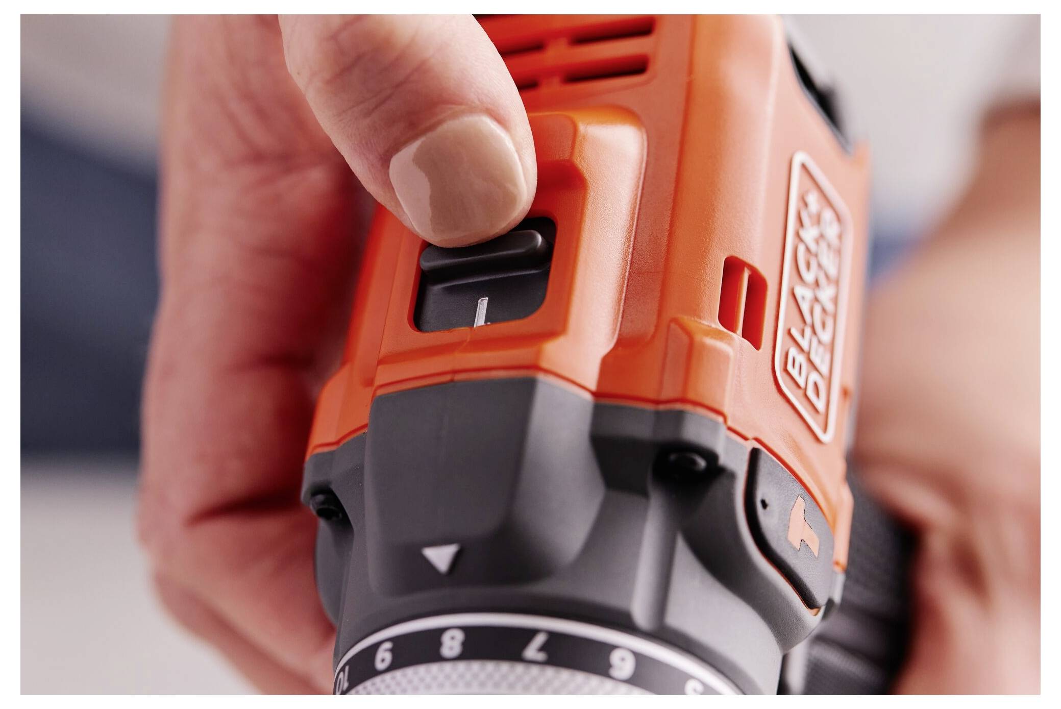 'Close-up of a hand adjusting the speed setting on an orange power drill. The logo reads Black+Decker.'