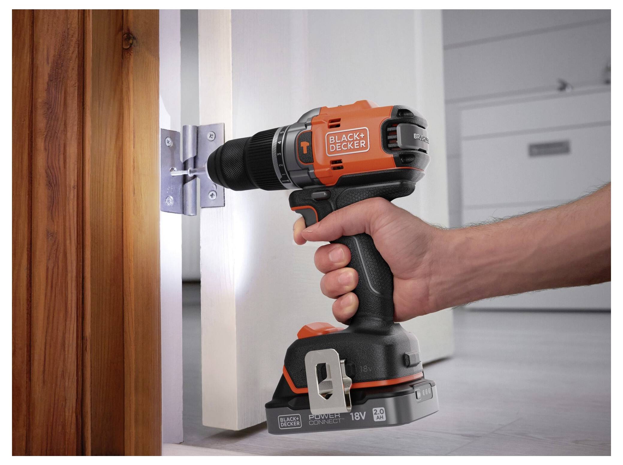 A hand uses an orange and black cordless drill to install a hinge on a wooden door, illustrating home repair or assembly.