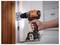 A hand uses an orange and black cordless drill to install a hinge on a wooden door, illustrating home repair or assembly.