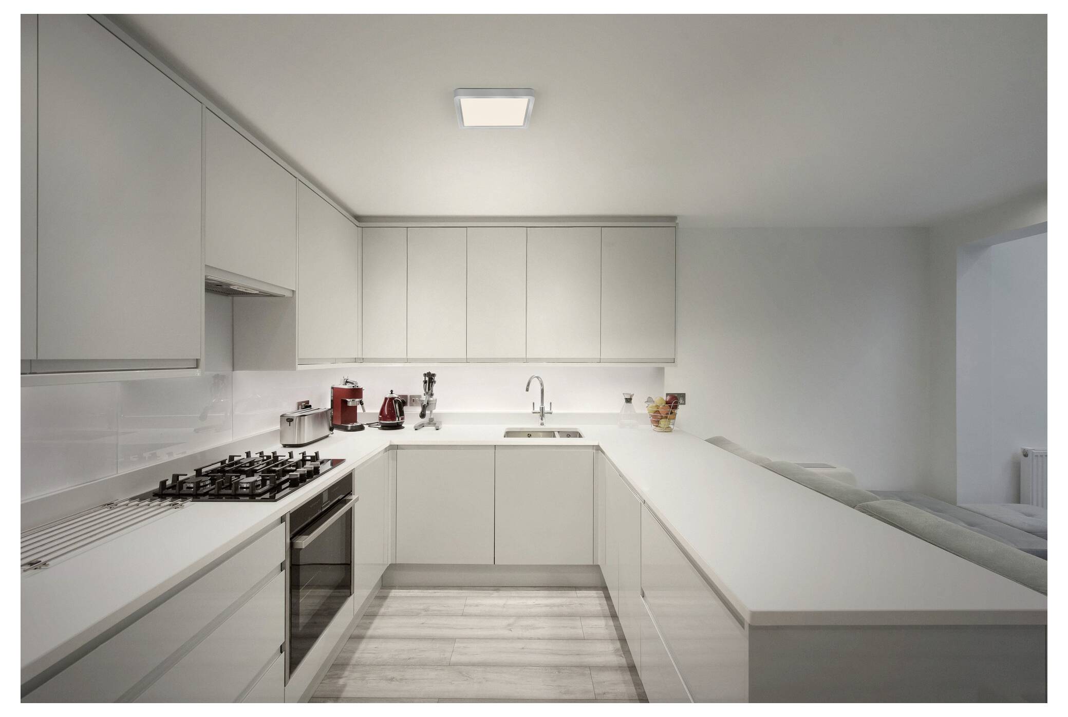Modern white kitchen with sleek cabinets, built-in stove, and stainless steel appliances on a wooden floor. Bright lighting illuminates the space.