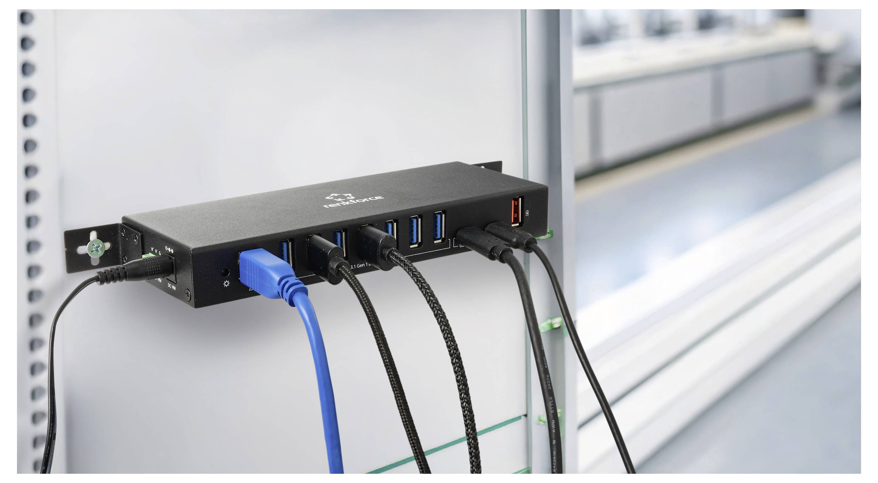 Black industrial device mounted on a wall with multiple connected cables and USB ports, likely a network hub or controller in a technical setting