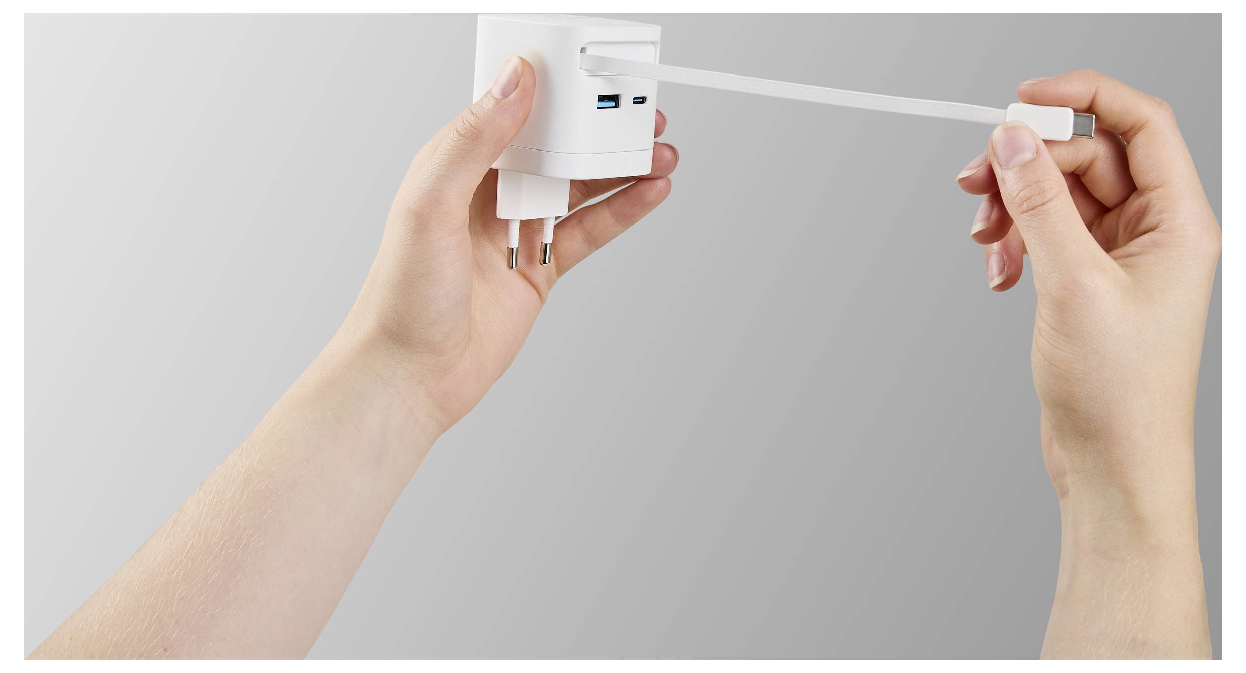 A person extends a retractable charging cable from a plug adapter, demonstrating the adapter's functionality against a neutral gray background.