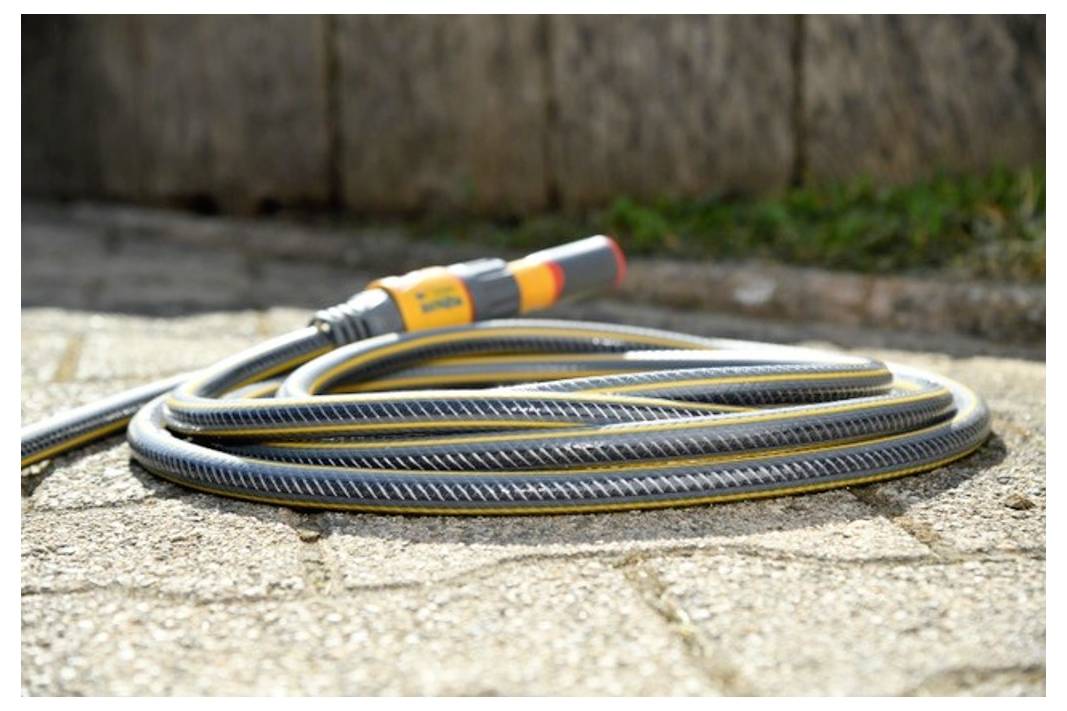 A coiled garden hose with an adjustable nozzle lies on a sunlit stone patio.