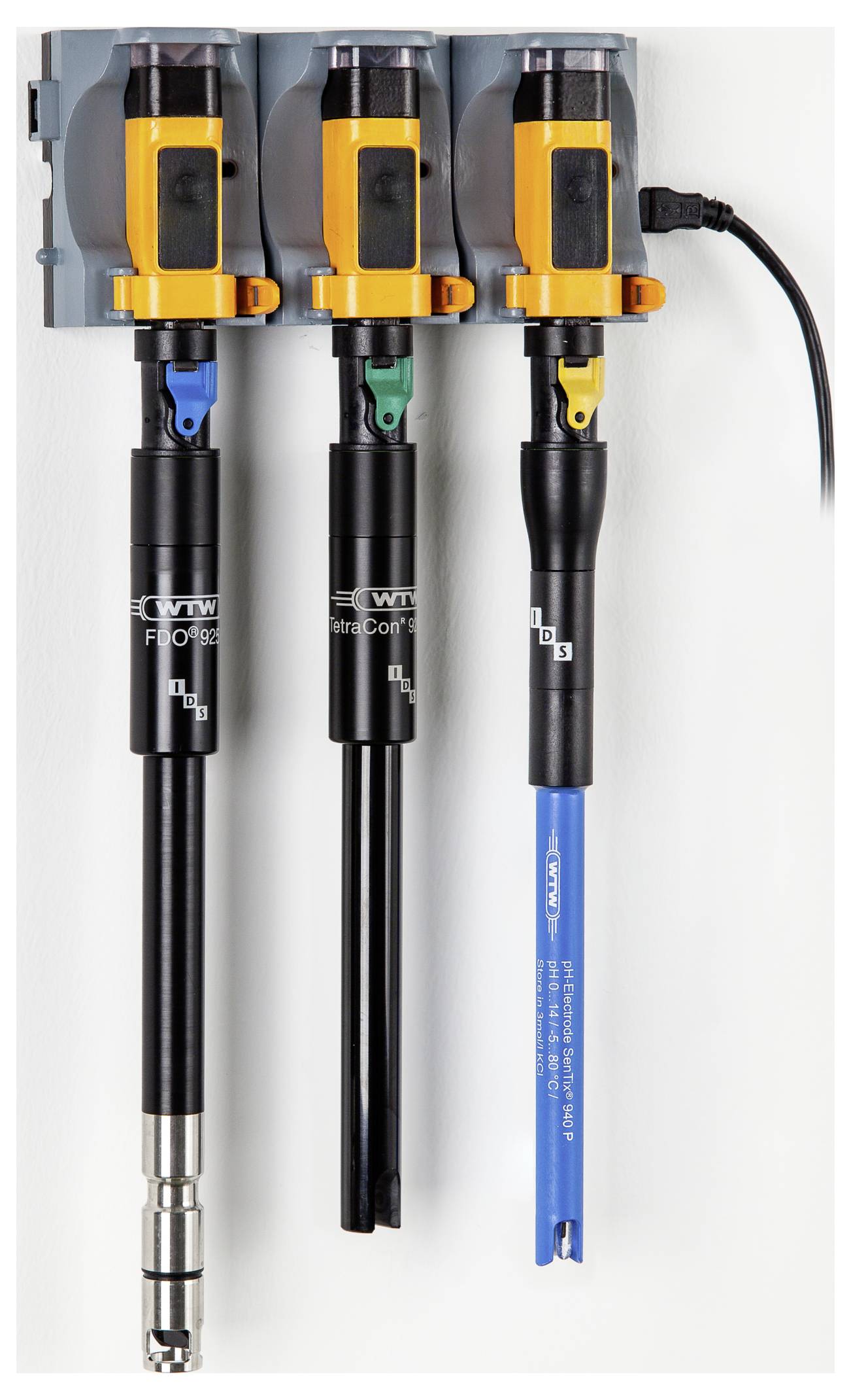 Three sensors are mounted vertically on a wall, each with a distinct colored top: orange, green, and blue, connected by cables.