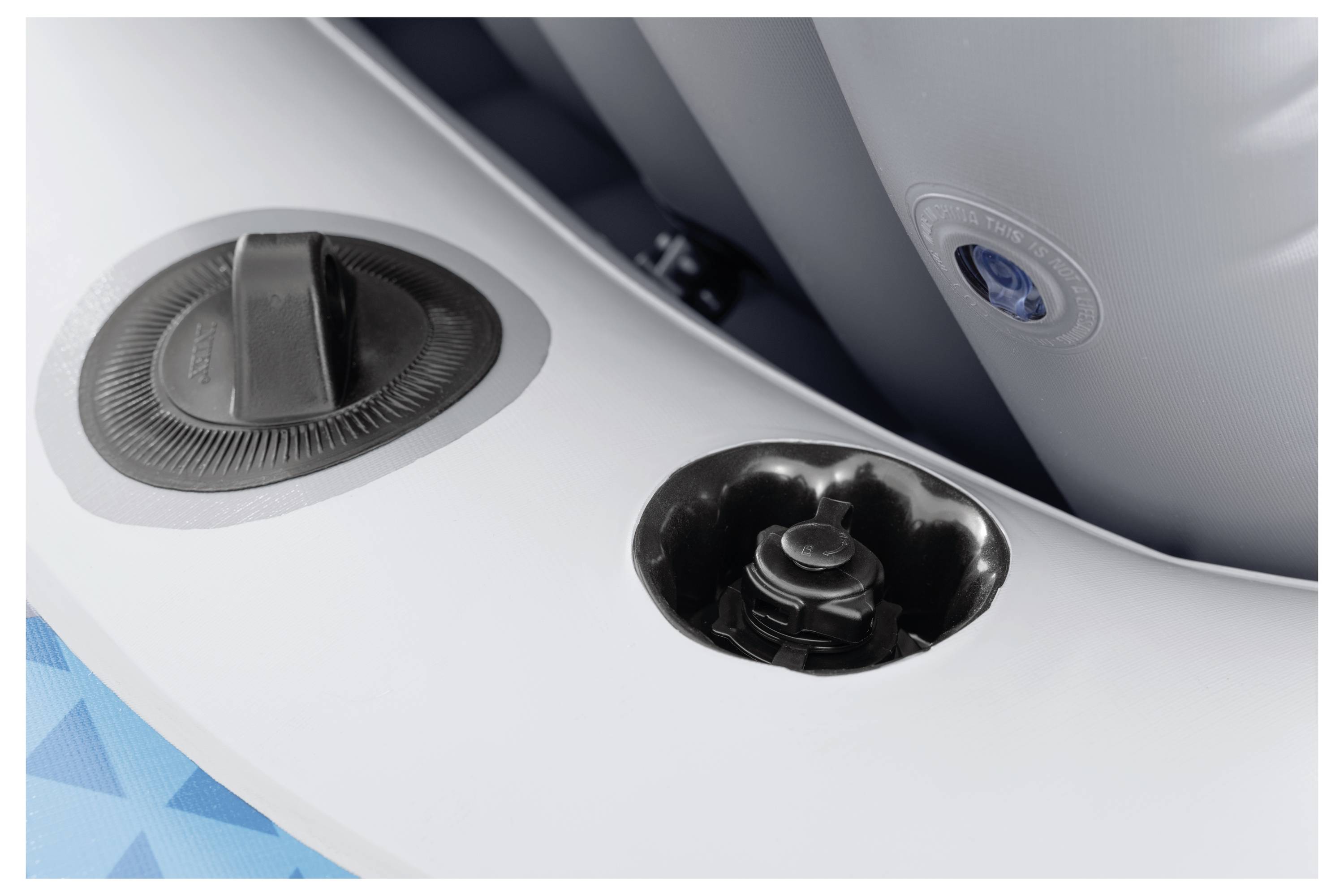 'A close-up of an inflatable air valve and cap on a grey inflatable object. A partial view of a blue patterned section is visible.'
