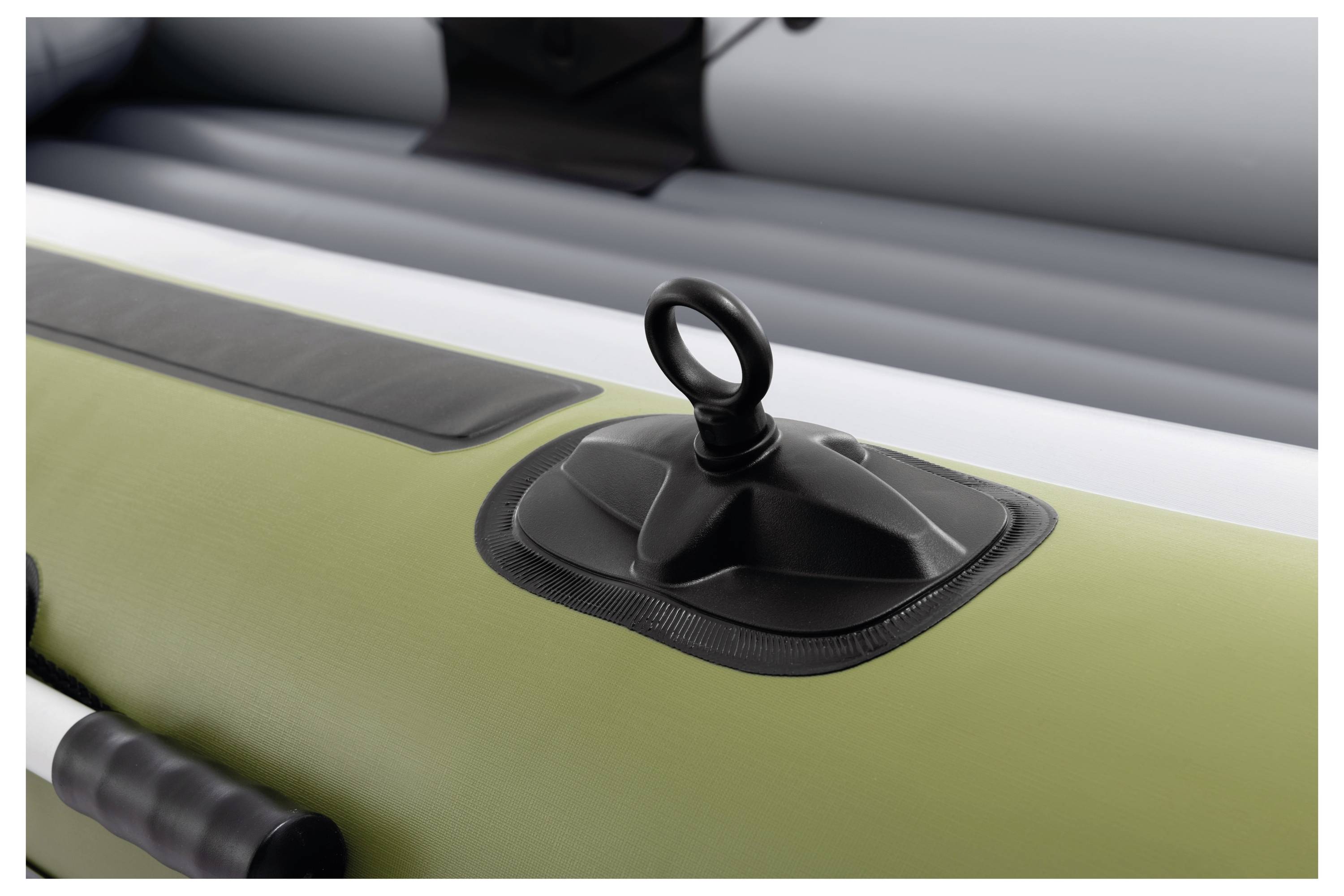 Close-up of an air valve on an inflatable boat, showing a black ring and cap on a green and gray surface.