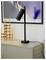 A black desk lamp with a modern design rests on a light-colored cabinet. Decorative gold candleholders are beside it, under framed artwork.