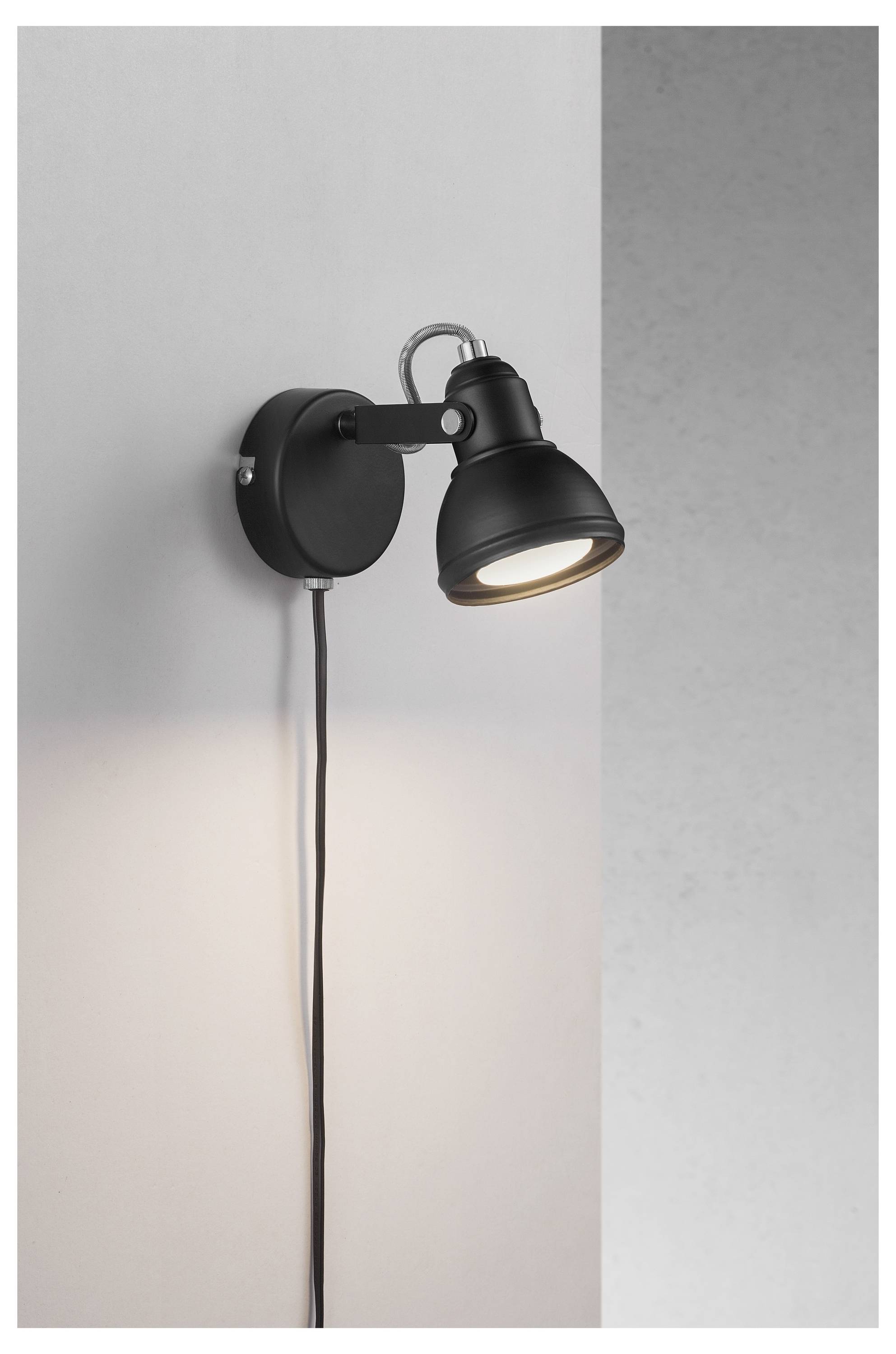 A black wall-mounted spotlight illuminates a grey wall.