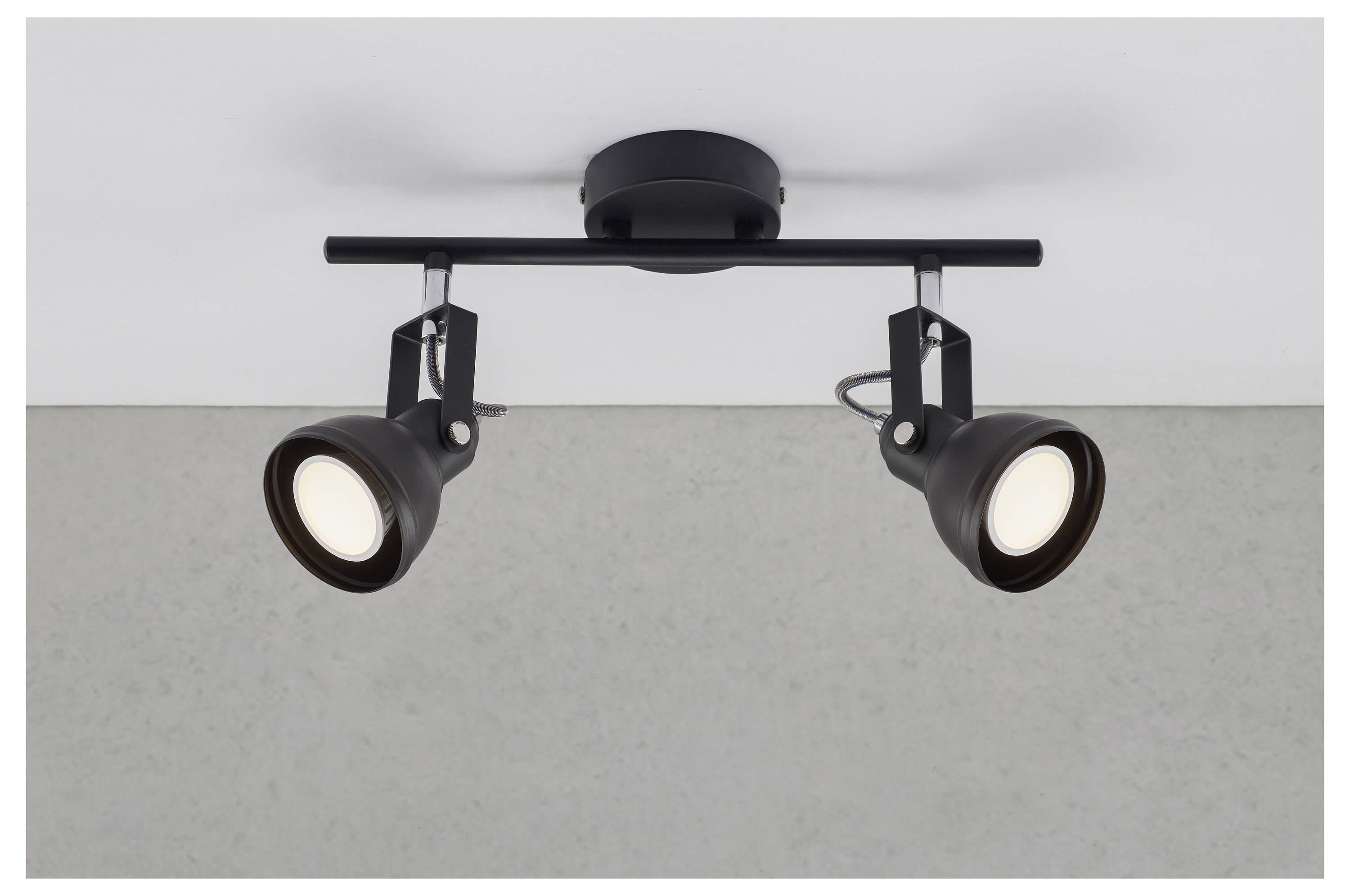 A ceiling-mounted light fixture with two adjustable, round spotlights directed downwards, providing focused illumination in a room.