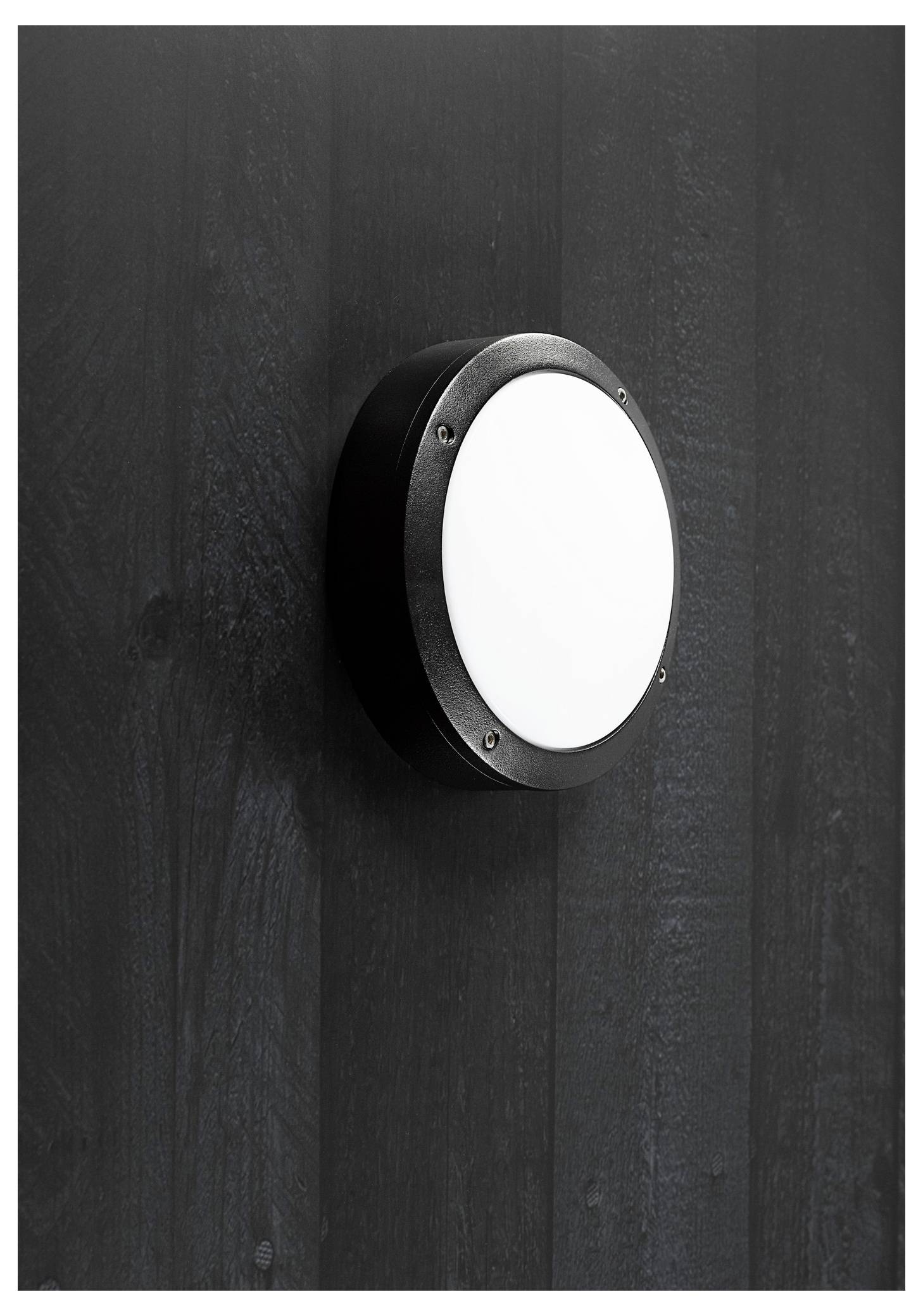 A round, modern black wall light with a white center, mounted on a textured dark wall. The design is minimalist and sleek.