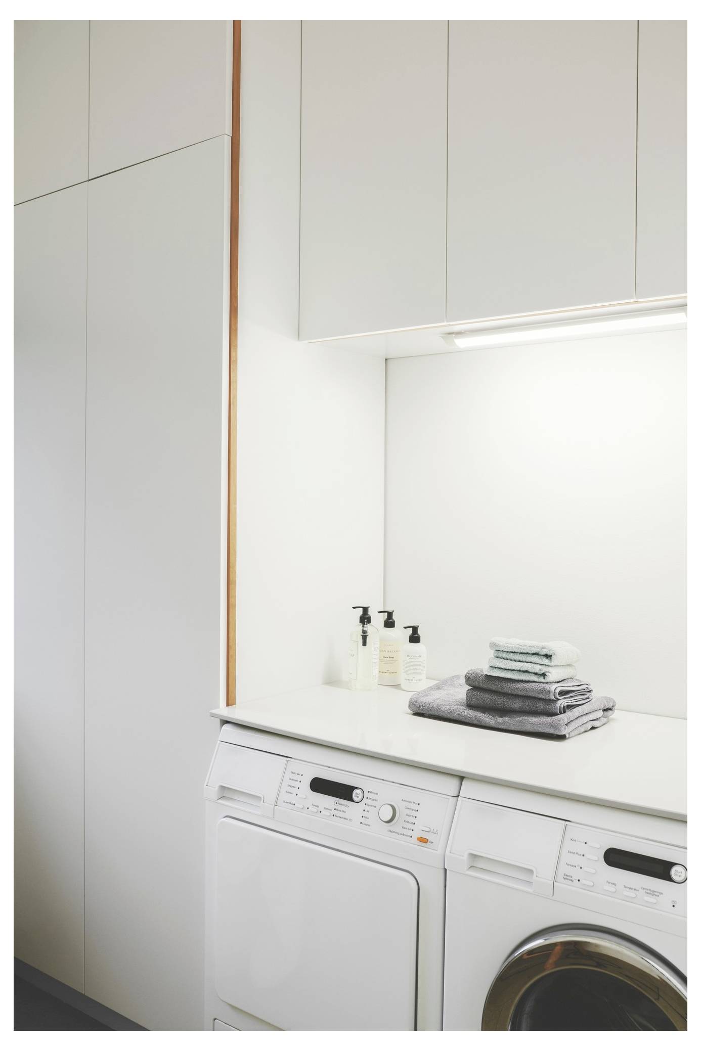 A clean laundry room with a washing machine and dryer, neatly folded towels on top, and two soap dispensers beside them. Brightly lit space.