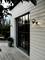 A modern house exterior with large glass doors, wooden siding, and outdoor wall lighting. A wooden deck and potted plant are visible.
