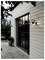 A modern house with wooden siding and a glass door, framed by outdoor wall lights. A small deck and potted plant are visible.