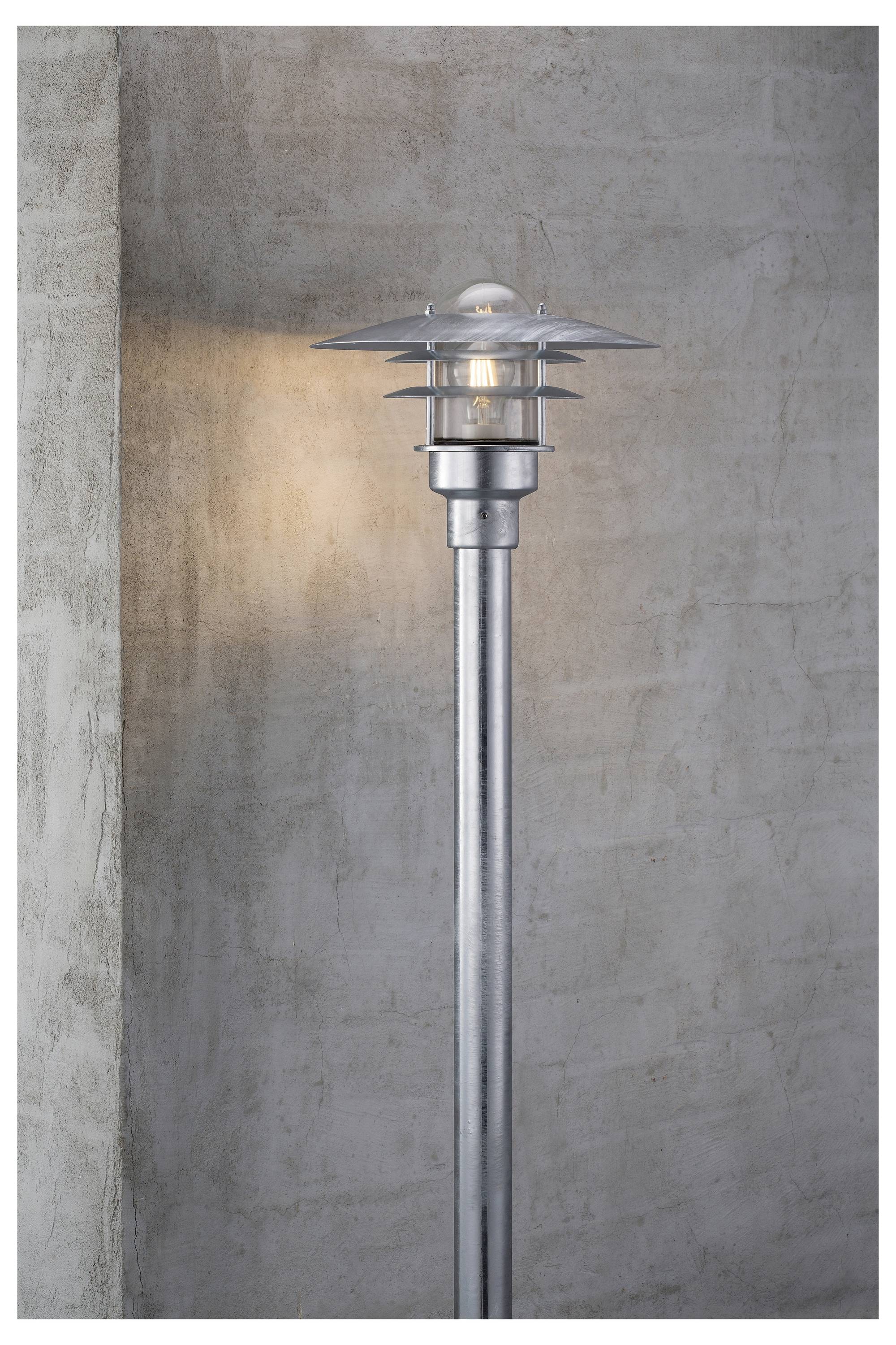 A modern outdoor wall lamp with a metallic finish mounted on a concrete wall, casting a soft, warm glow on the surface.