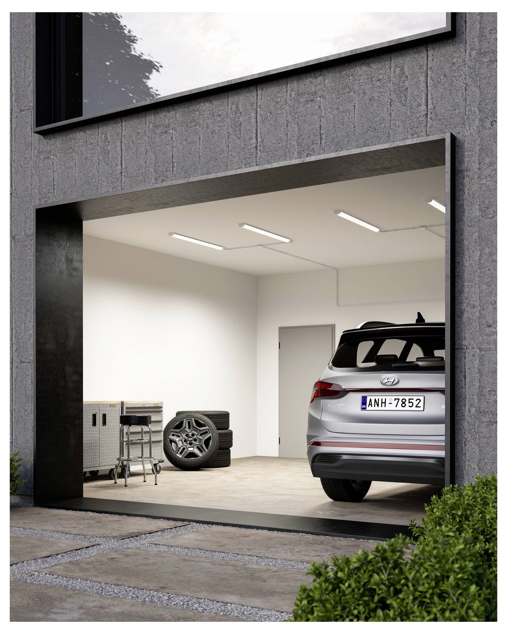 A gray SUV is parked in a modern, clean garage with a concrete wall. There's a tool chest and a set of spare tires on the left side.