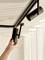 A hand adjusting a black ceiling-mounted track light near white curtains, highlighting interior lighting adjustment.