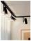 Track lighting fixtures on a white ceiling in a modern interior, with one fixture lit and framed artwork partially visible below.
