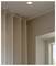 A beige curtain hanging in the corner of a room next to a window, with a ceiling light turned on, creating a cozy atmosphere.