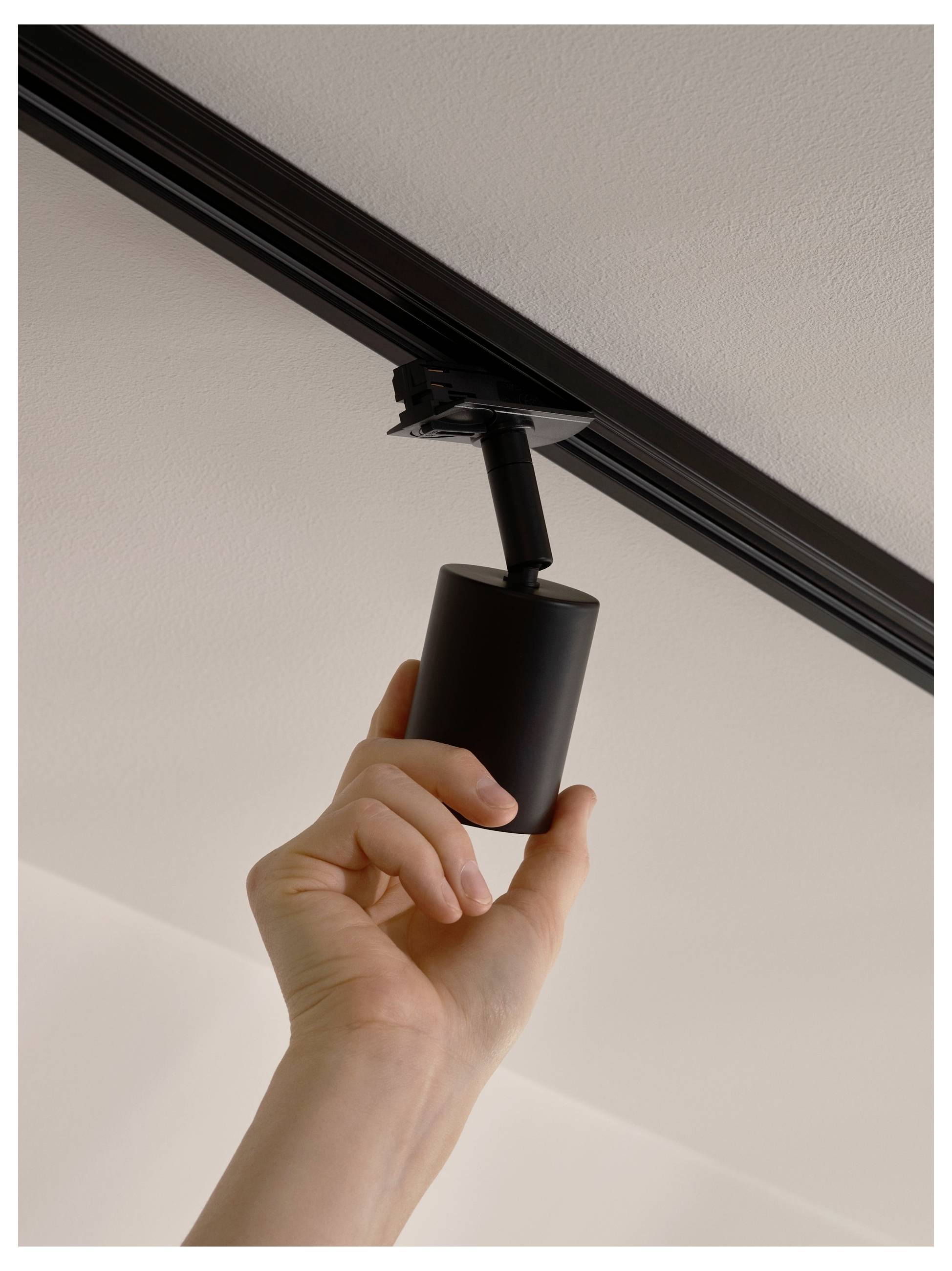 A hand installing or adjusting a black ceiling-mounted spotlight, emphasizing home or office lighting setup.