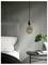 A gray bedroom with a modern hanging light, a bed with white linens, and a round table holding books and a potted plant.