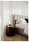 A cozy bedroom features a bed with neutral bedding and a tufted headboard. A wooden nightstand holds a lit lamp and a small book.