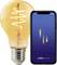 A smartphone displaying the 'nordlux smart' app next to an orange LED light bulb with a visible spiral filament, illustrating smart lighting control.