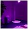 A dimly lit room with a smart speaker and a modern lamp casting purple light on a table, next to an open book.