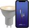 A smart light bulb next to a smartphone displaying the 'nordlux smart' app interface with colored vertical bars, indicating connectivity.