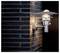 A modern wall light fixture with a metallic finish illuminates a dark brick wall, casting a soft glow.