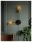 Modern wall sconce with two glowing bulbs on a dark green paneled wall; nearby, a brown chair and a large leafy plant add decor elements.