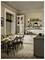 A cozy kitchen with wooden flooring, a dining table set for breakfast with sunflowers and fruit, white cabinets, and shelves with kitchenware.