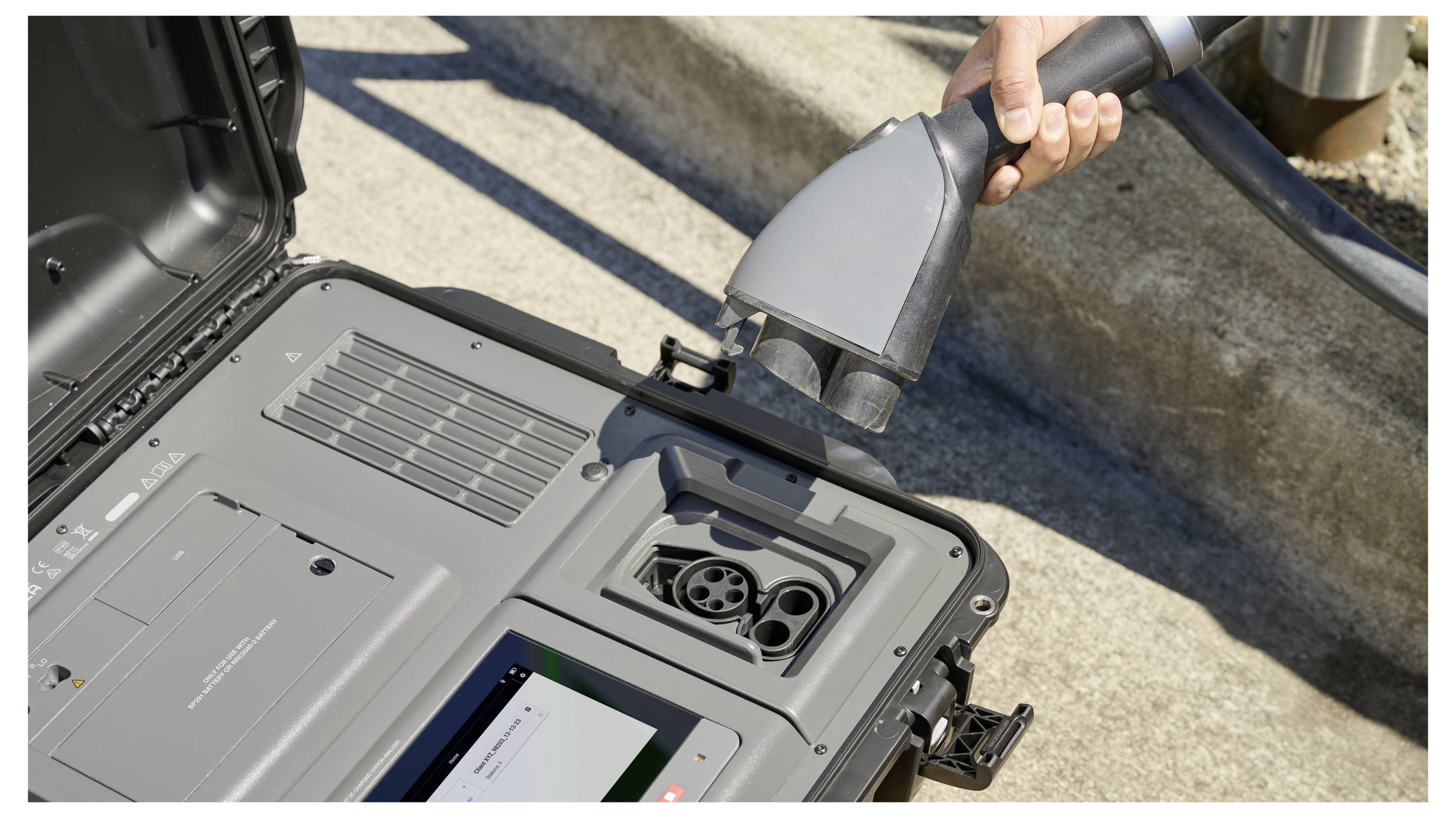 A person holds an electric vehicle charging connector near a portable charging station, showcasing its plug and outlet design.