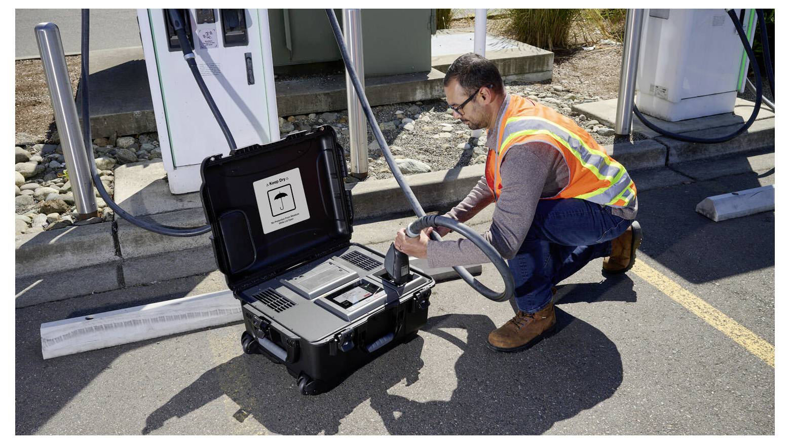 A person wearing a safety vest is inspecting or operating equipment in a portable case at a charging station, suggesting maintenance work.