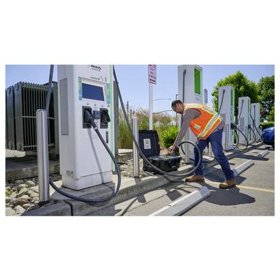 A worker in a safety vest inspects electric vehicle charging stations, connecting cables from a black equipment case, outdoors on a sunny day.