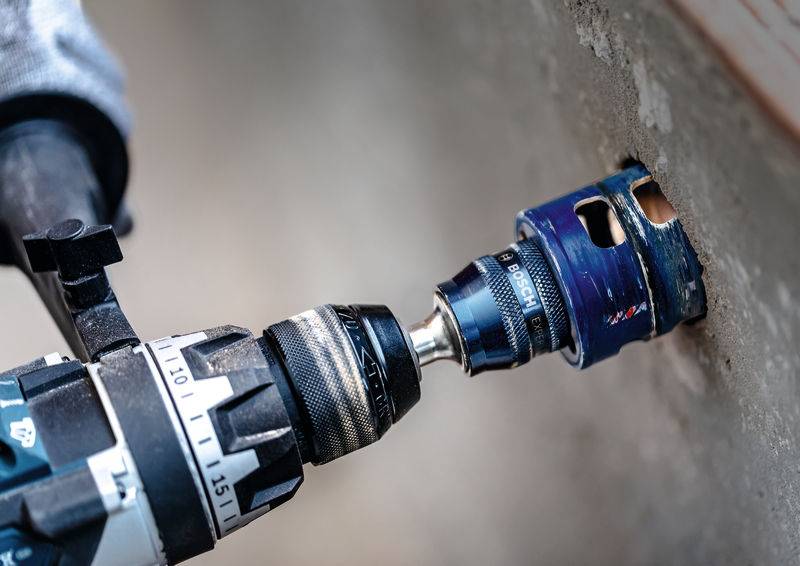 'A drill with a hole saw attachment is cutting through a concrete wall.'