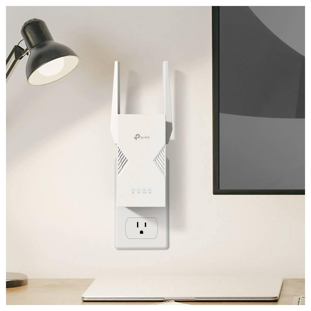 A Wi-Fi range extender is plugged into a wall socket next to a desk with a lamp and laptop, enhancing wireless internet coverage.