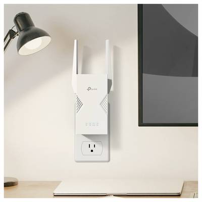 A Wi-Fi range extender is plugged into a wall socket next to a desk with a lamp and laptop, enhancing wireless internet coverage.