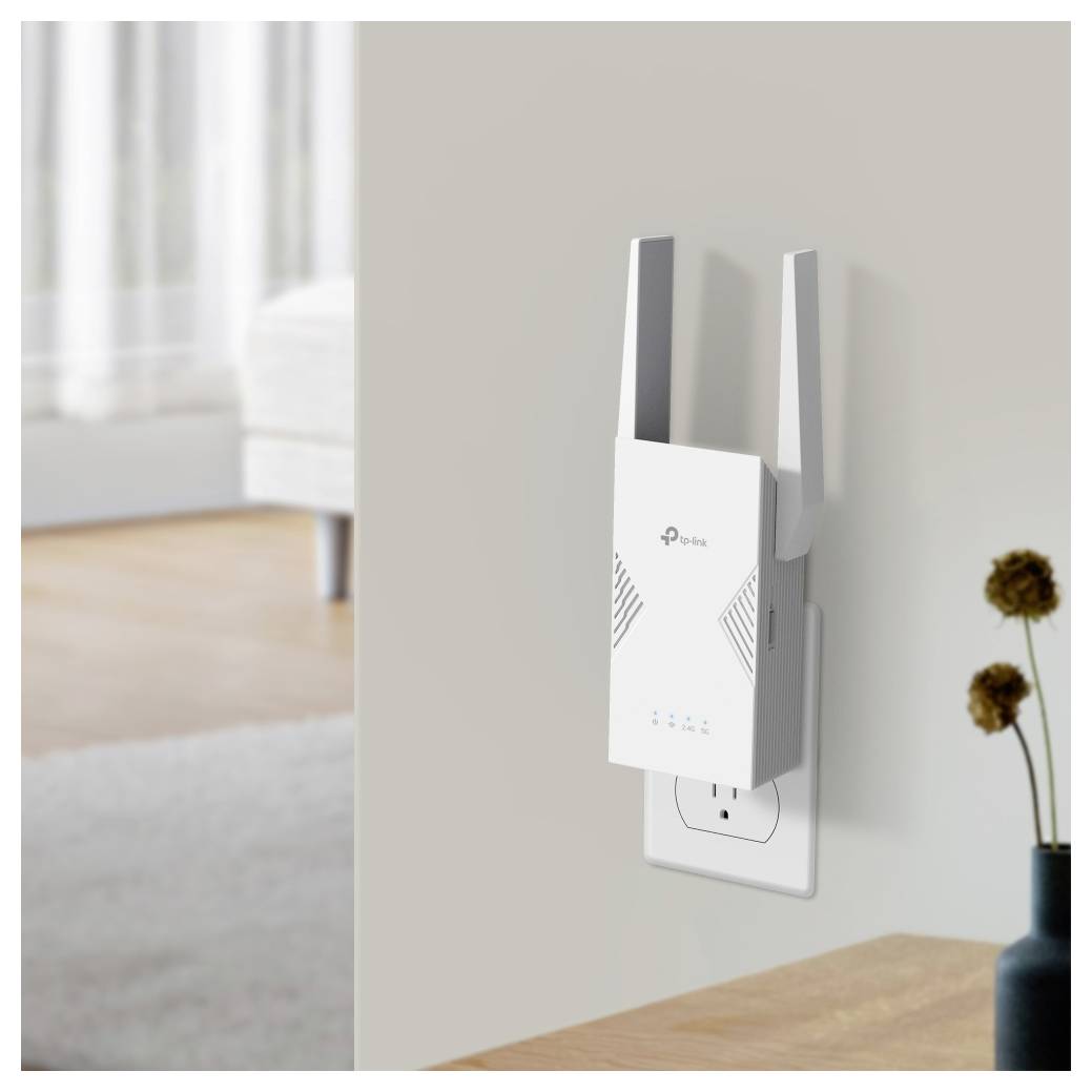 A white Wi-Fi range extender plugged into a wall outlet, with indicator lights on, in a bright living room setting.