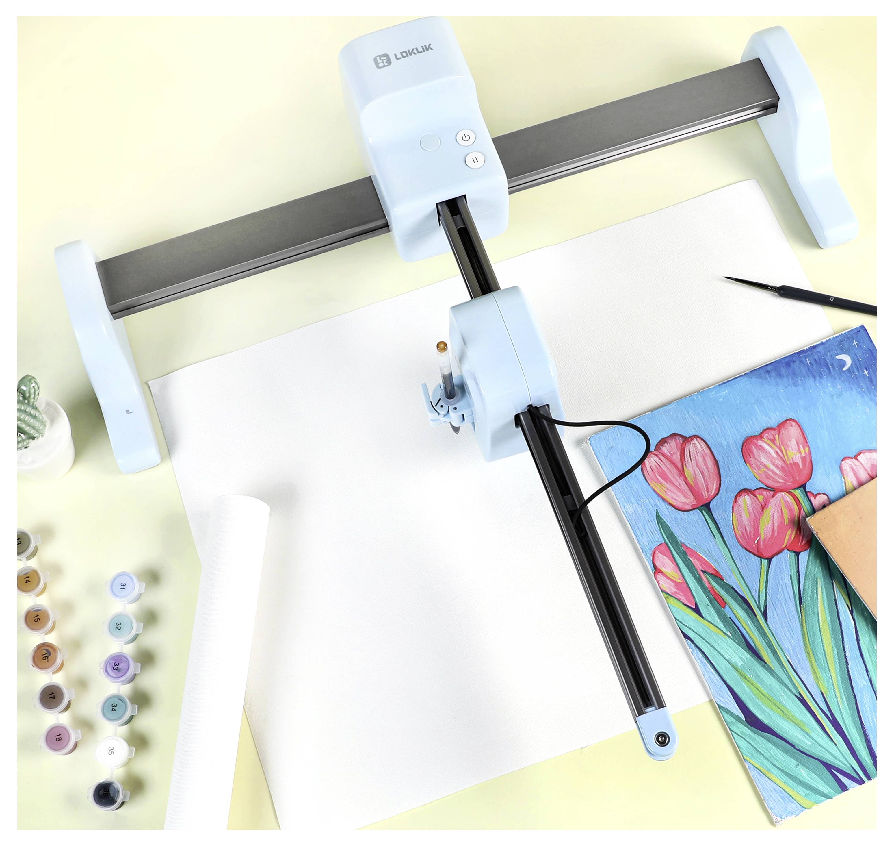 A drawing machine positioned above a blank sheet, with a finished artwork of pink tulips and art supplies like paints and brushes nearby.