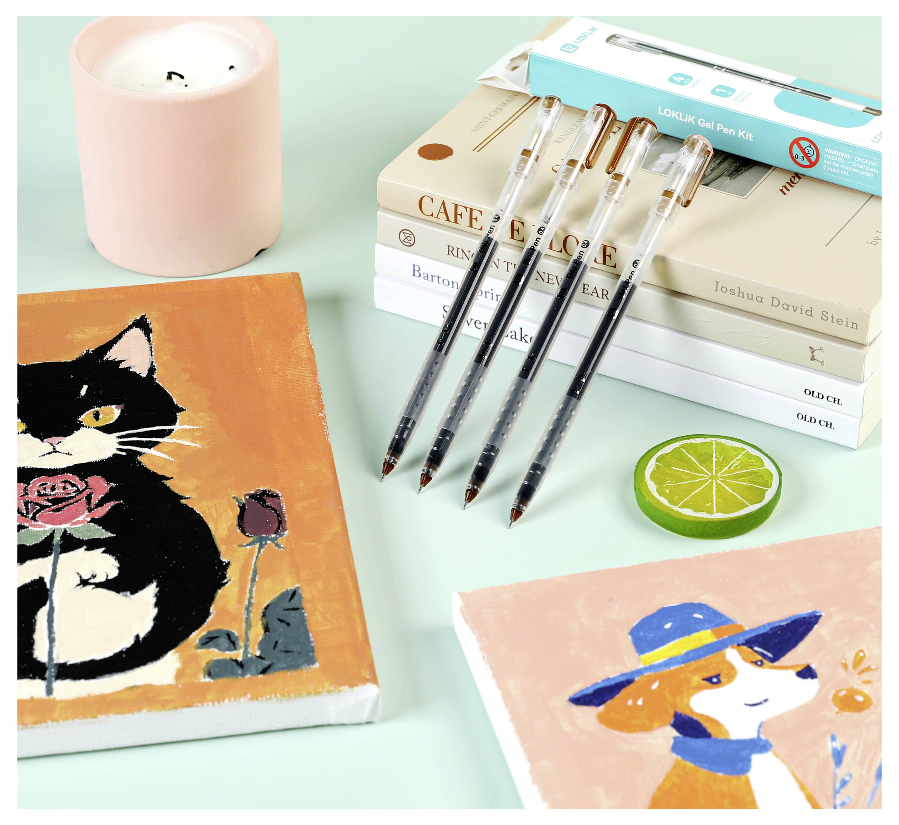 'Art supplies and books on a desk; includes paintings of a cat with a rose, a dog with a hat, pens, a candle, and stacked books.'